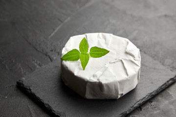 Camembert cheese with basil on black slate board over dark concrete background