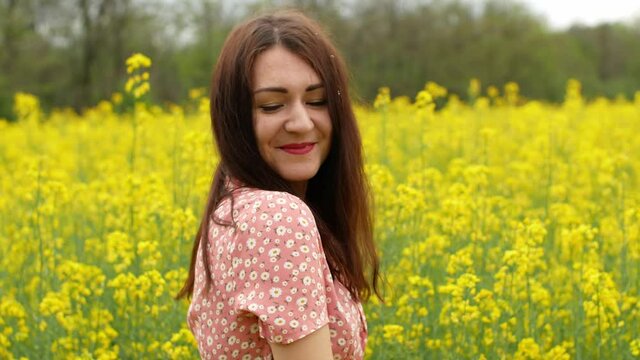 A beautiful cheerful young girl takes pictures of herself on the phone in a field against a background of yellow rapeseed flowers. A girl in a dress walks through a field of spring flowers.

