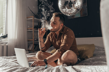 Man blowing out puffs of smoke and smoking weed hand rolled cigarette - obrazy, fototapety, plakaty