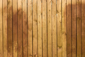 A fence made of wood planks treated with an antiseptic. There are two large patches of dark brown paint and small debris from paper notices. Background. Texture.