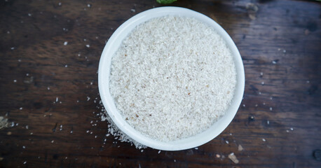 Psyllium husks on white small plastic bowl on wooden board top view