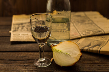 Glass of vodka with  newspaper and onion with bottle on an old wooden table. Angle view, shallow depth of field