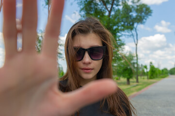 pretty woman in sunglasses makes a hand gesture to prohibit taking pictures.