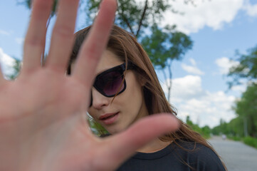 pretty woman in sunglasses makes a hand gesture to prohibit taking pictures.