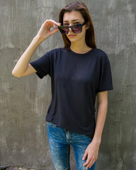 young beautiful woman in sunglasses and loose hair on the background of a gray wall straightens her glasses.