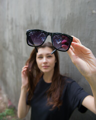 young beautiful woman with loose hair holds sunglasses in her hands and examines them.