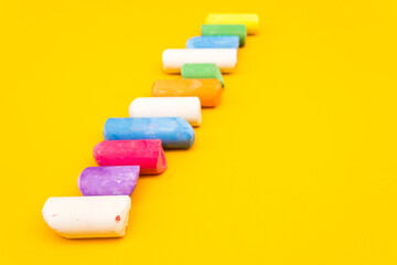 Children's drawing crayons lie in a row on a yellow background. Multi-colored chalk close-up.