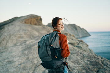 woman in a red sweater in the mountains on nature and a backpack on her back blue sea sky autumn