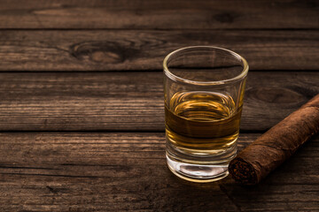 Glass of tequila with cuban cigar on an old wooden table. Close up view