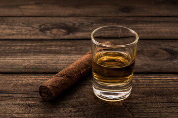 Glass of tequila with cuban cigar on an old wooden table. Close up view