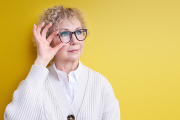 mature woman with serious and concentrated confident look, brainstorming and thinking about challenging problem, posing isolated on yellow, wearing elegant outfit and eyeglasses