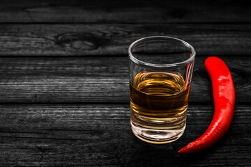 Glass of tequila with cayenne pepper on an old wooden table. Close up view