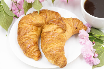 Croissants on a white plate and a cup of coffee on a background of delicate flowers. Top view.