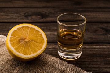 Glass of tequila with piece of cloth and half a lemon on an old wooden table. Close up view