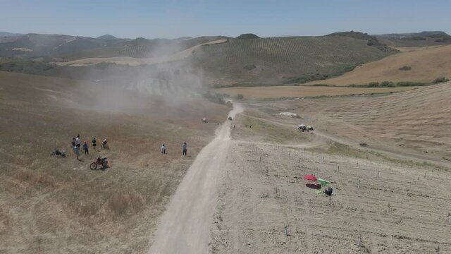 Aerial drone tracking shot of rider racing in a rally race speeding into the desert with dust and smoke trails.