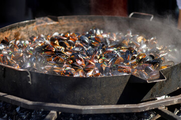 Delicious mussels boiling in big bowl, cooking seafood at open air kitchen. Preparing yummy mussels at street food festival. Summertime. Summer vacation picnic
