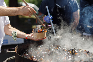 Chef putting delicious boiled mussels in take away box, cooking seafood at street food festival....