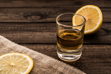 Glass of tequila with piece of cloth and a slice of lemon on an old wooden table. Close up view