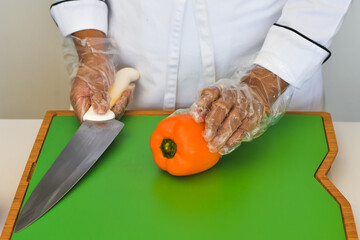 chef con guantes desechables multiusos antes de cortar una rodaja de chile morrón color naranja...
