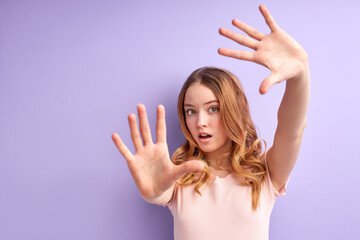 Young girl over isolated purple background scared with arms up like something falling from above,...