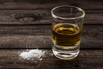 Glass of tequila with salt on an old wooden table. Close up view