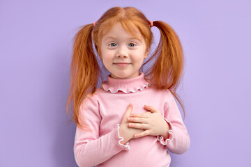 Caucasian little girl looking at camera and holding hands on heart gesture of love. Studio portrait...