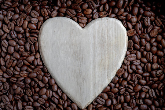 Selective focus of dark brown roasted coffee beans texture pattern background, Close up details of dried coffee beans with free copy space in the middle as heart shaped.