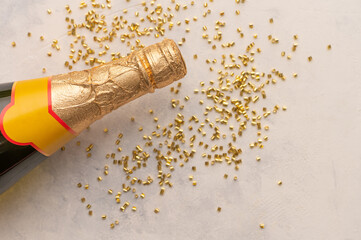 Obraz premium The photo shows a fragment of a bottle of champagne in a bright gold wrapper. Nearby is confetti. White background. Spirit of Christmas. Holiday spirit. White background. Place for your insert.