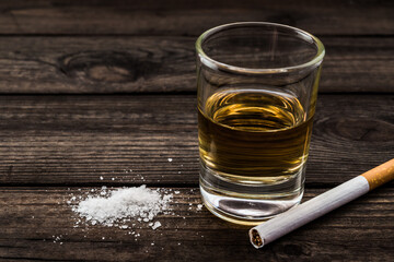 Glass of tequila with salt and cigarette on an old wooden table. Close up view
