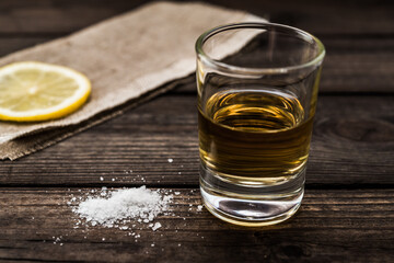 Glass of tequila with piece of cloth and a slice of lemon with salt on an old wooden table. Close up view, shallow depth of field