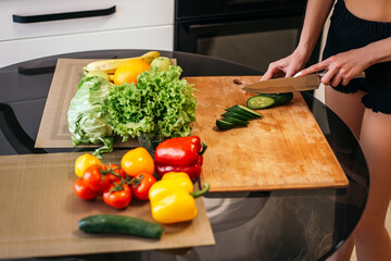 Pretty blond woman standing kitchen hold hand cut chopping cucumber products fruits vegetables wooden cutting board. Lady preparing breakfast lunch after training, want cook healthy food, copyspace.
