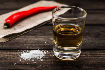Glass of tequila and piece of cloth with cayenne pepper and salt on an old wooden table. Close up view, shallow depth of field