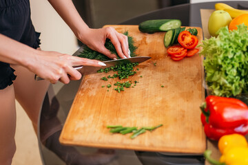 Close up shot woman standing kitchen chopping green salad dill plant products fruits and vegetables wooden cutting board. Lady preparing breakfast lunch after training, cook healthy food, copyspace.