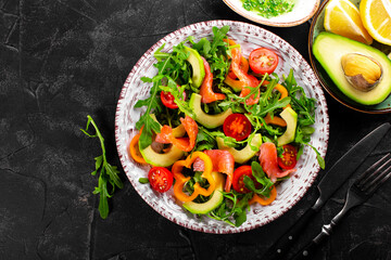 Fresh summer vegetable salad with arugula, tomatoes, bell peppers, avocado and salmon on a plate top view, photo with free space for text