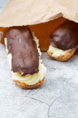 Chocolate eclair with a custard cream filling in a brown paper bag. Environmentally friendly packaging for recycling