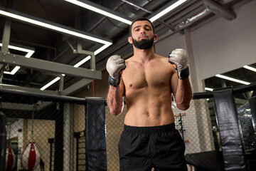 Fototapeta na wymiar Portrait of MMA fighter thinking about strategy for match, standing on ring preparing for fight, shirtless muscular male is going to practice fighting