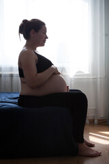Calm pregnant woman sitting in bed at home bedroom and enjoyng the pregnancy