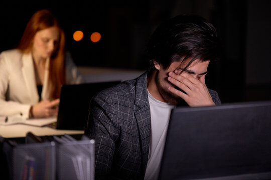 Tired And Overworked Business Man Manager Sitting In Front Of Computer Laptop And Trying To Concentrate. Male Worker Eyes Are Dry And Hurt Painful. Young Guy Work In Night Office