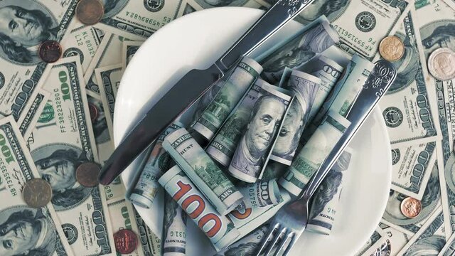 money. dollar bills and coins. close-up. rotation. hundred dollar bills and different coins background. plate with a pile of rolled dollar bills and cutlery, knife and fork