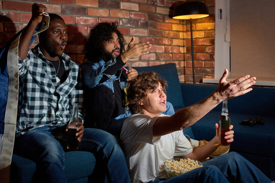 Emotional guys watching basketball sport match at home. Multiethnic group of friends, fans cheering for favourite national team, drinking beer. Concept of emotions, support, sport competition