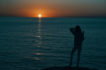 woman in the mountains at sunset near the sea raised her hands up