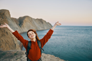 happy traveler in the mountains near the sea gestures with her hands and a backpack on her back