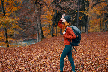 happy travel woman with backpack walks through the autumn park in nature near the river landscape tall trees sweater