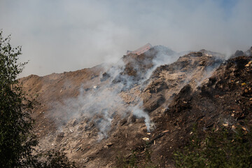 smoke from a burning landfill. harmful to the environment toxic and acrid smoke in the air. plastic burns, releasing greenhouse gases into the atmosphere. an environmental disaster. a high mountain of
