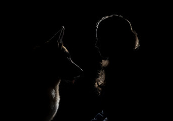 Silhouette of dog and woman illuminated by bright light on black background. Profile of German...