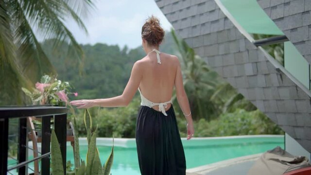 Young woman walks on the terrace outdoors of exotic summer villa, she dressed in black dress