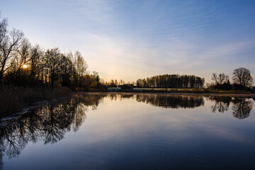 Naklejka na ściany i meble trees by the water with sky reflections