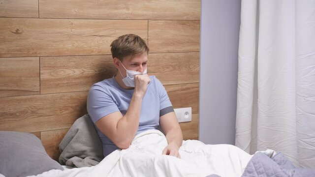 Man has respiratory symptoms fever, coughing, body aches sitting on bed at home alone, suffering from bad disease. Quarantine, self-isolation, healtcare concept.