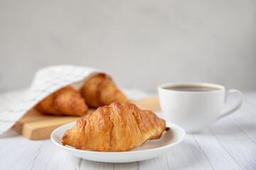 Concept food. Delicious fresh croissants on a plate and a cup of coffee next to. Light background.