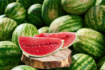 A juicy ripe watermelon, cut up, lies on a pile of other watermelons. Red watermelon looks delicious lying in the sun on other watermelons.